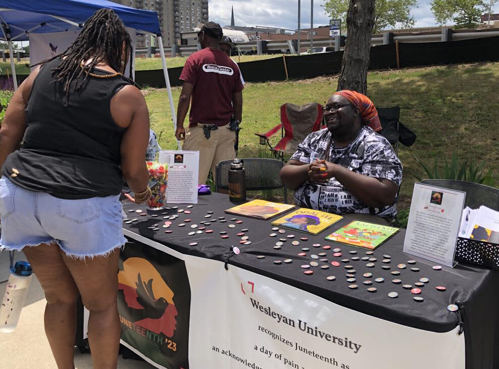 Wesleyan community members staffing a table at the Liberation Day Festival in Middletown, including Demetrius Colvin, Director of the Resource Center, Adjunct Instructor of Education Studies, and member of the Wesleyan Planning Committee for Juneteenth. (Andrew Chatfield MALS ’19)