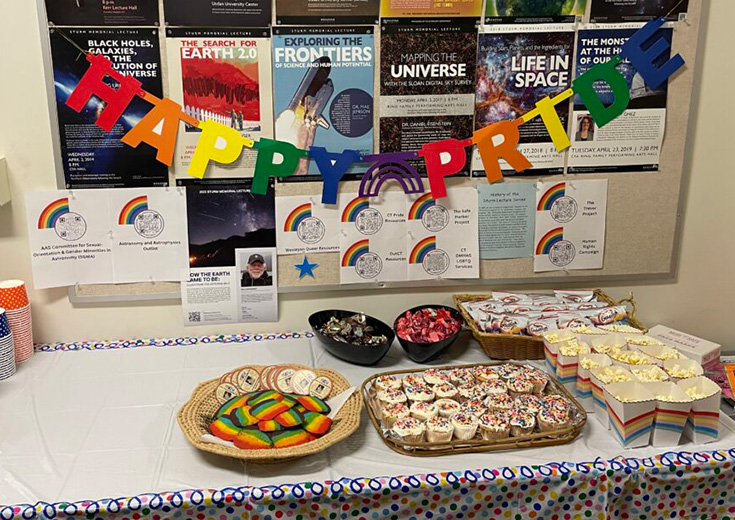 A “Happy Pride” banner hangs above rainbow treats and posters celebrating LGBTQ+ inclusion in astronomy.