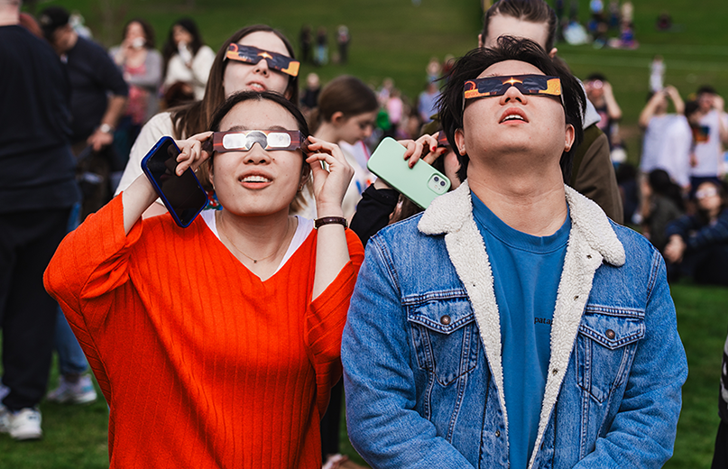 Students wearing eclipse glasses look up at the sky during a solar eclipse viewing event.