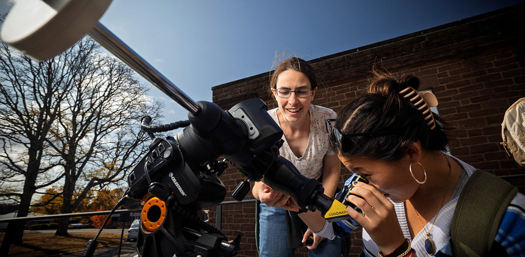 A student looks through a small solar telescope while another person assists during a public observing session.