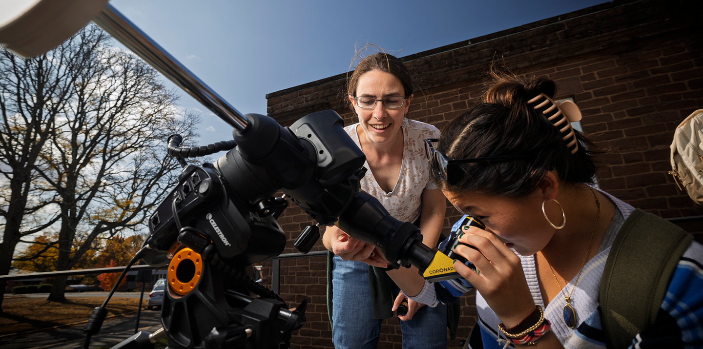 A student looks through a telescope outside of the observatory with an astronomy professor